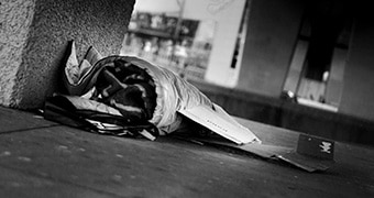 Black and white photo of a sleeping bag and cardboard box on the ground.
