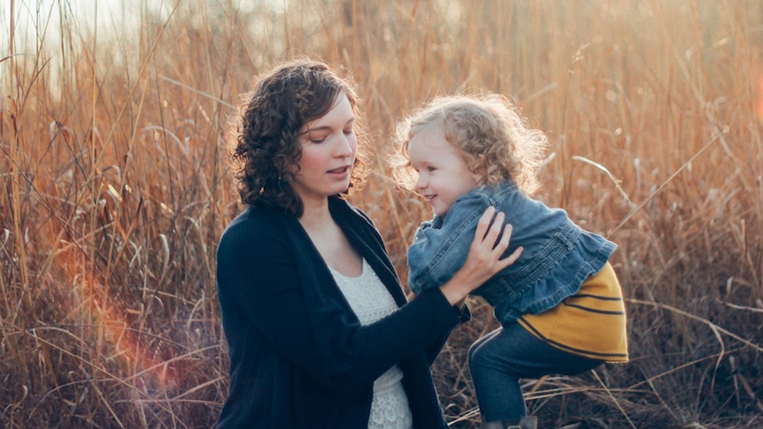 A mother holds her daughter while standing in long grass.