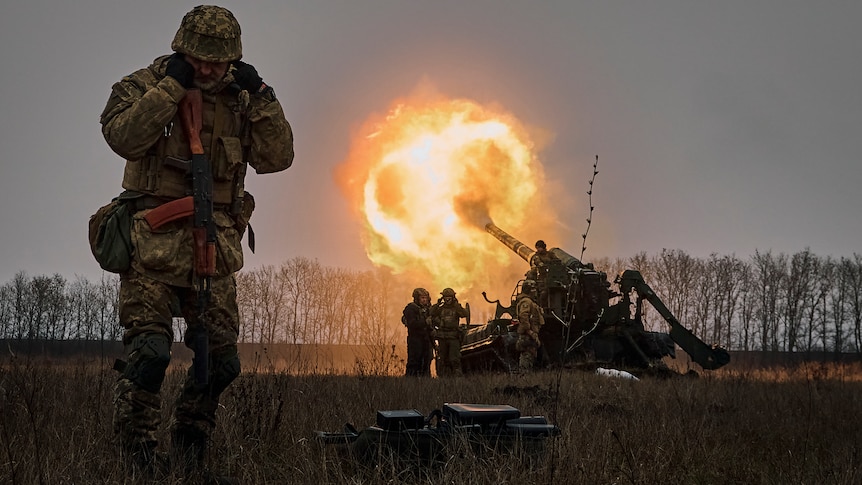 A Ukrainian soldier blocks his ears as others fire a Pion artillery system at Russian positions.