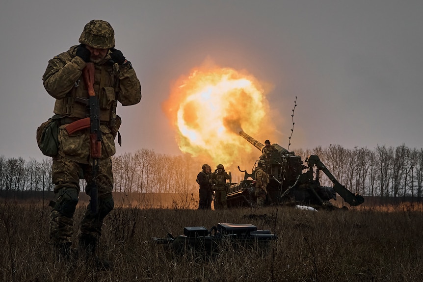 A Ukrainian soldier blocks his ears as others fire a Pion artillery system at Russian positions.