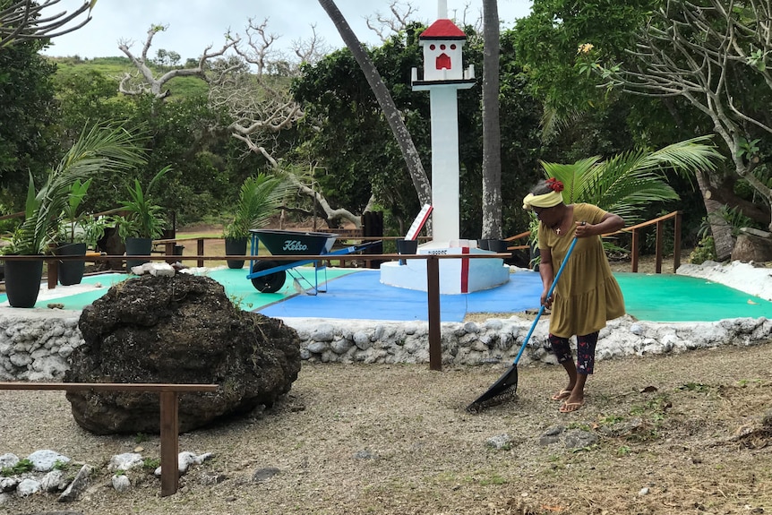 woman sweeps coral, behind her is a white cross