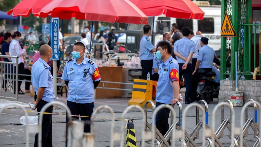police wearing face masks stand at the entrance to a street market