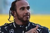 Lewis Hamilton looks behind over his left shoulder and holds his right hand in a thumbs up gesture