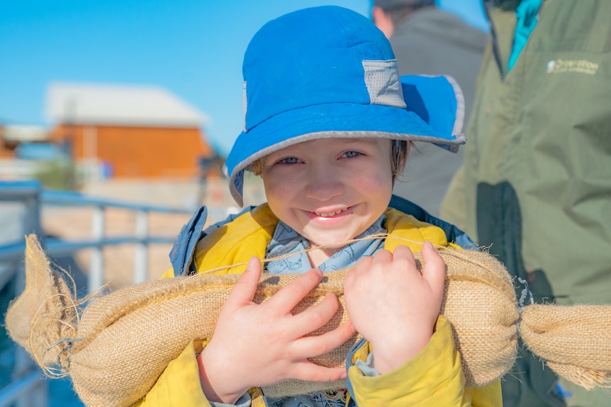 A boy in a blue hat carries an elongated hessian sack