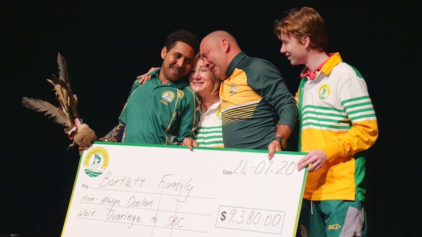 Alwyn Doolan, Cara Bartlett, Peter Bartlett and Caleb Bartlett huddle together emotional with a $9,380 cheque.