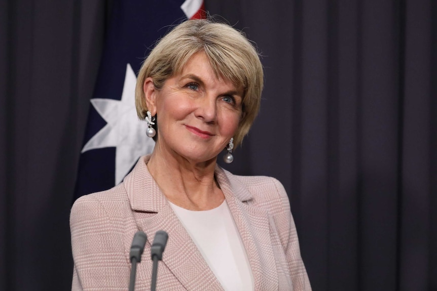 Bishop is smiling in front of an Australian flag.