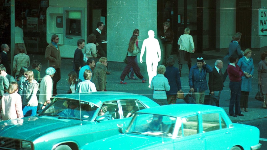 A white outline walks among pedestrians crossing and waiting in central Sydney.