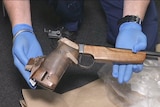 Two hands in blue gloves holding a gun.
