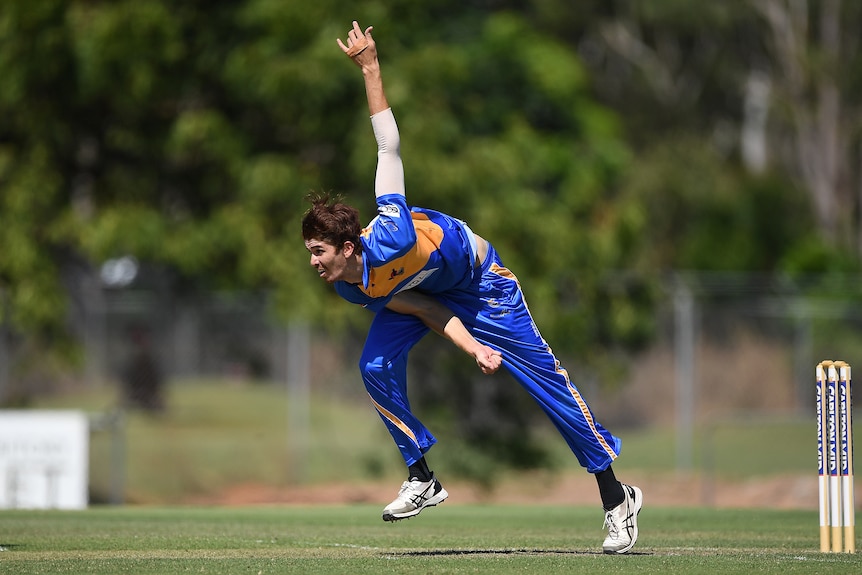 A man finishes his bowling action in blue and yellow cricket clothes.