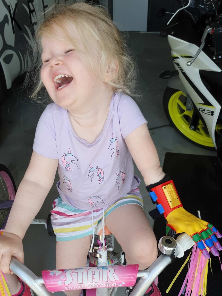 Izabella Carlson has a big smile on her face as she sits on her pink bike with her left prosthetic arm holding the handle bar.