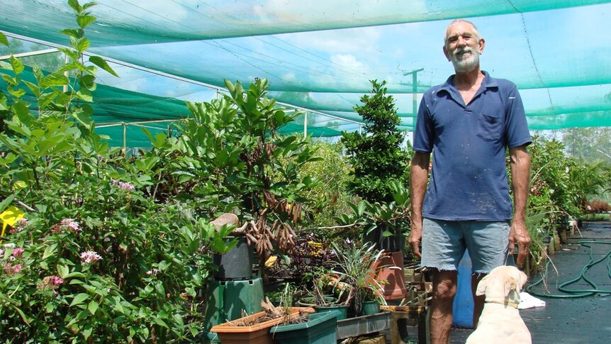 Steven Rose standing with his dog in front of plants growing in his nursery