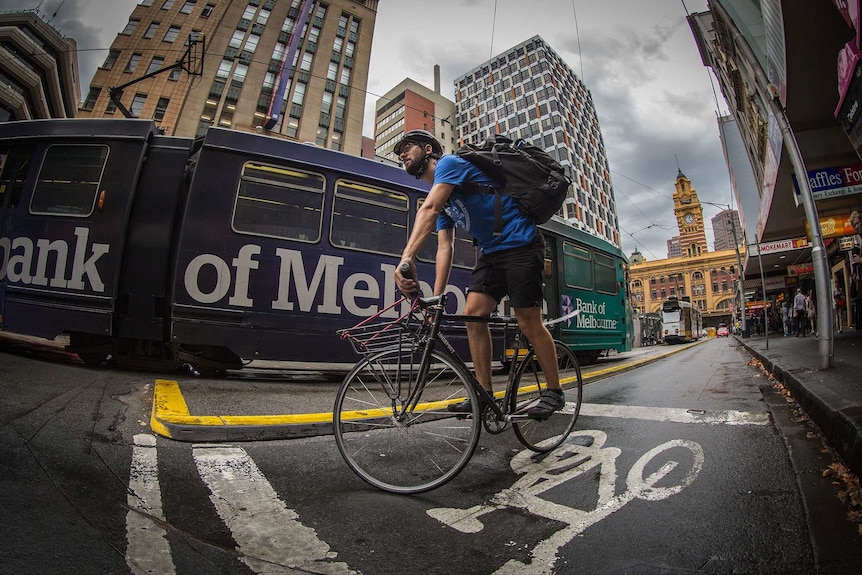 Wide-angle shot from low to the ground looking up at a man with a large backpack on a bicycle