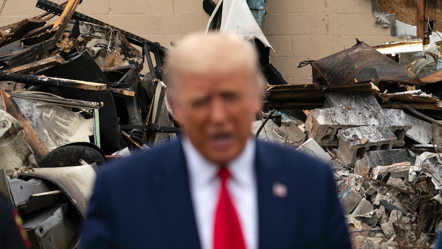 President Donald Trump speaks with damage in the background.