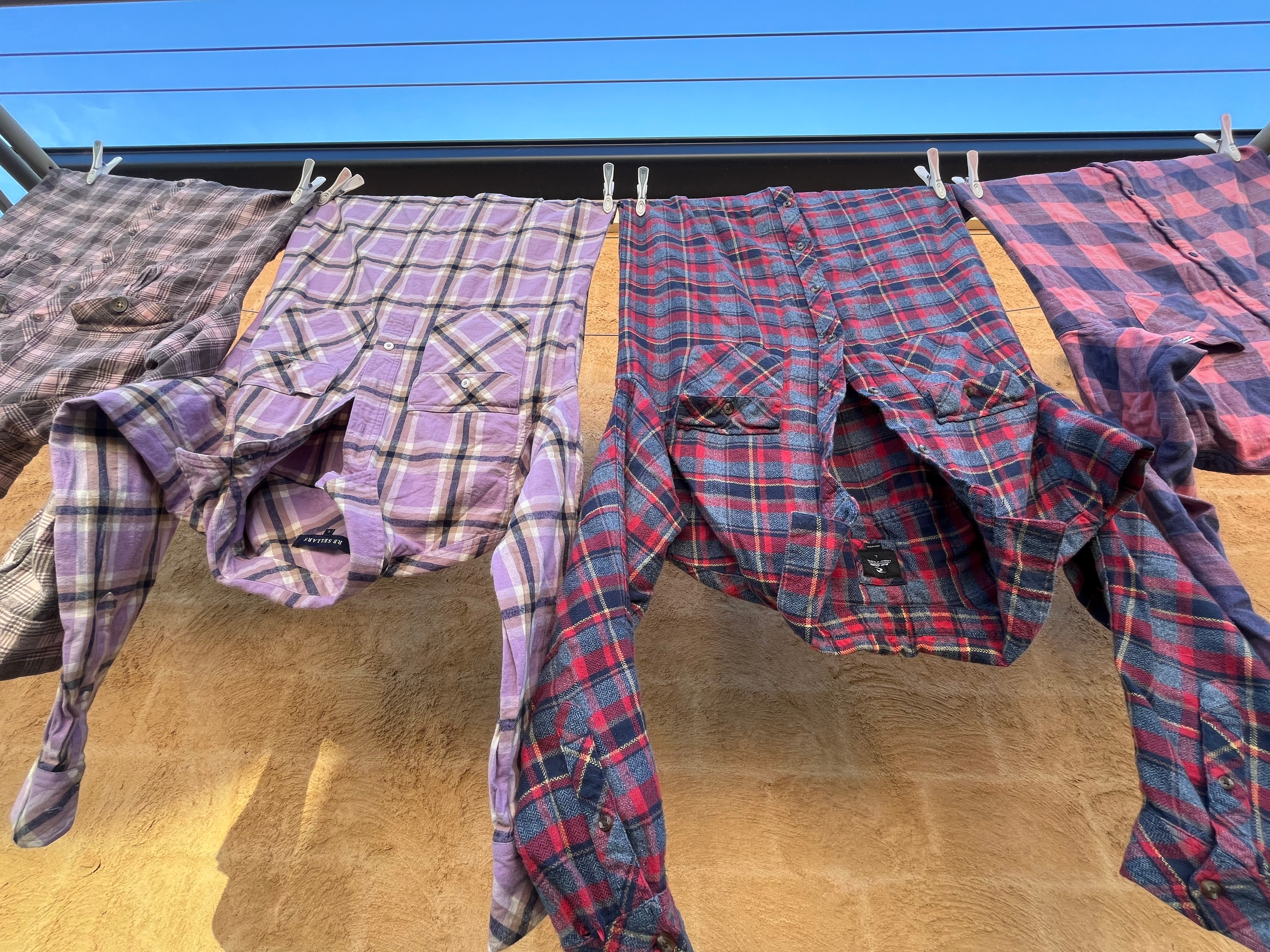 Cuatro camisas de franela en rojo, morado, rosa y azul cuelgan de un tendedero