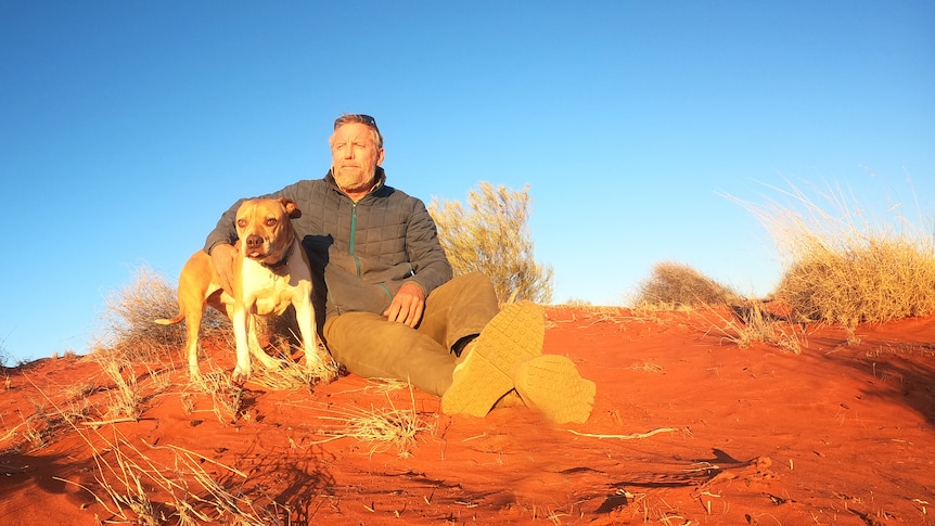 man and dog sitting in the desert