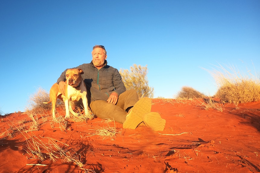 man and dog sitting in the desert