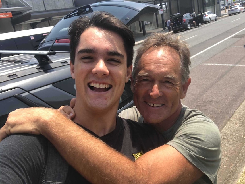 A young man being hugged by an older man in a busy street.