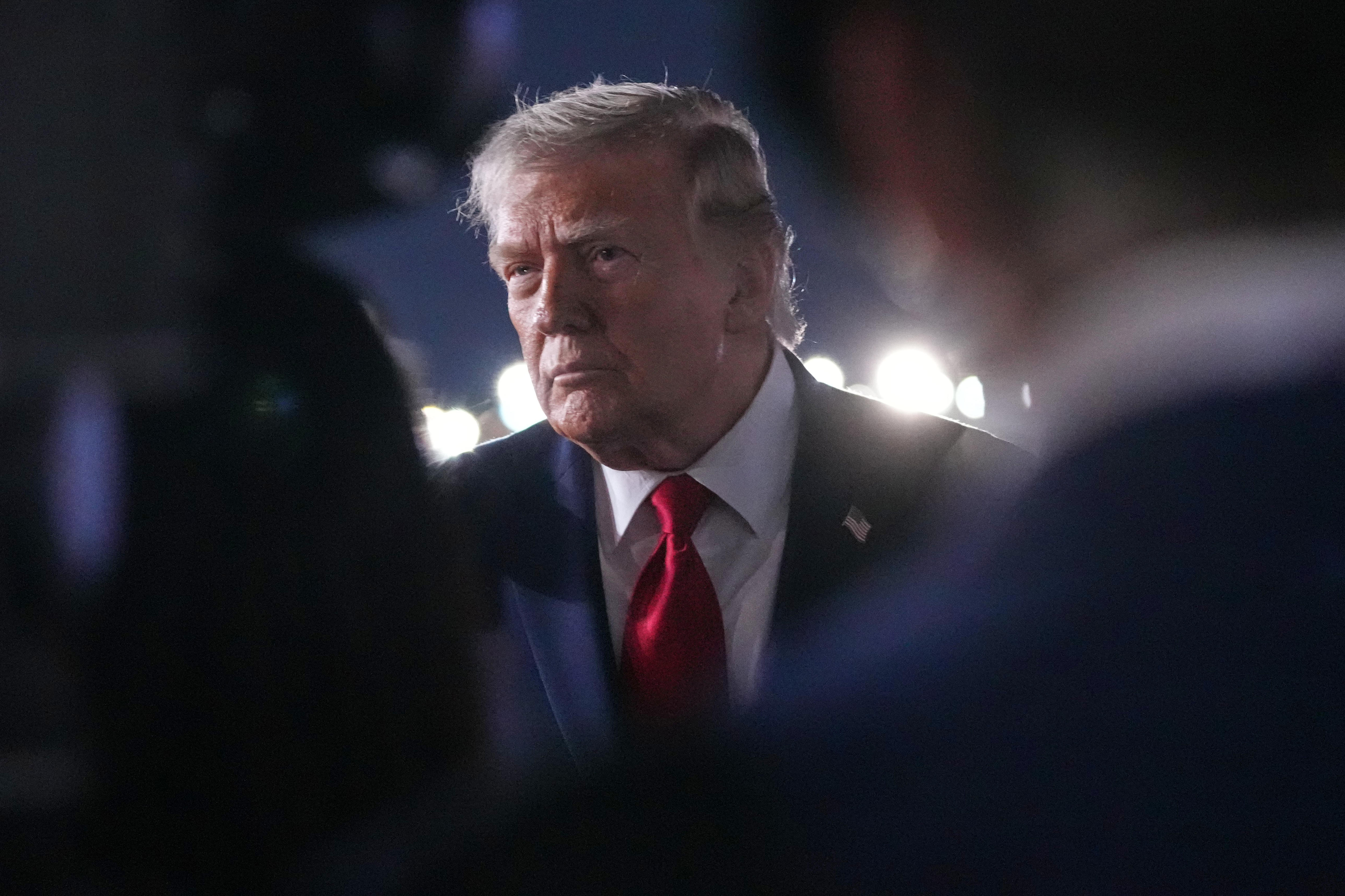 A nighttime image of a man with a red tie standing in front of reporters