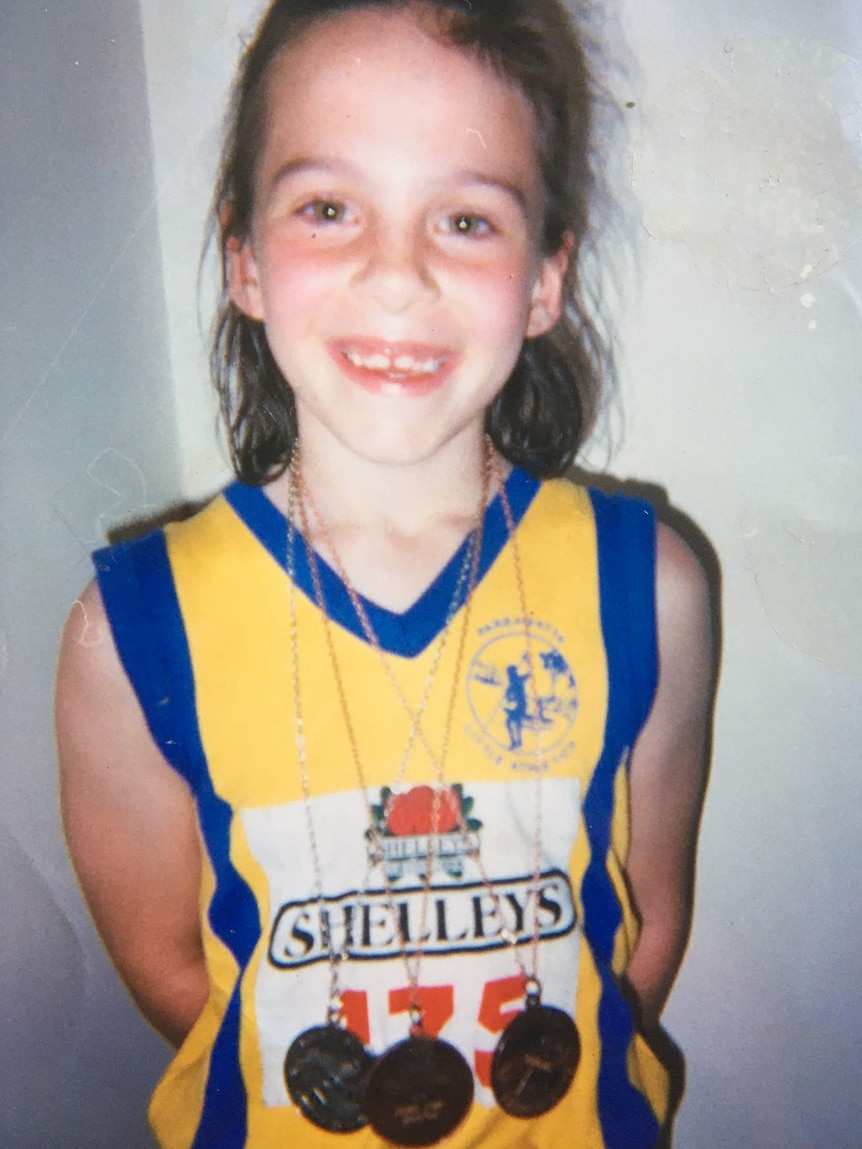 A young Rebecca smiles while posing with three medals around her neck.
