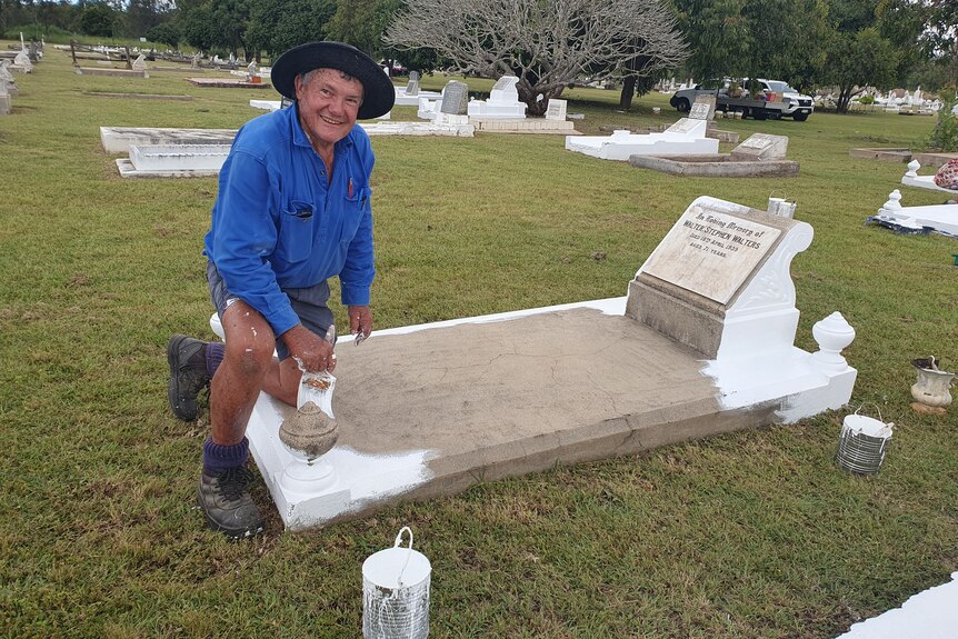 Man painting grave and smiling at camera