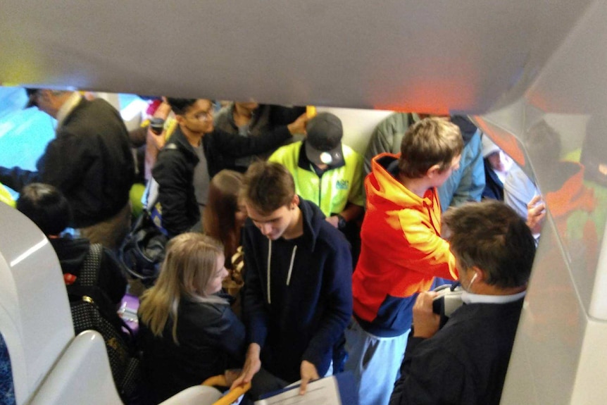 A train carriage full of people with standing room only, people squashed in next to each other.