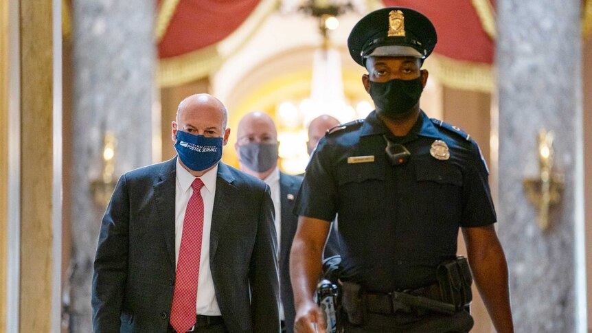 Louis DeJoy walks with a security guard wearing a mask