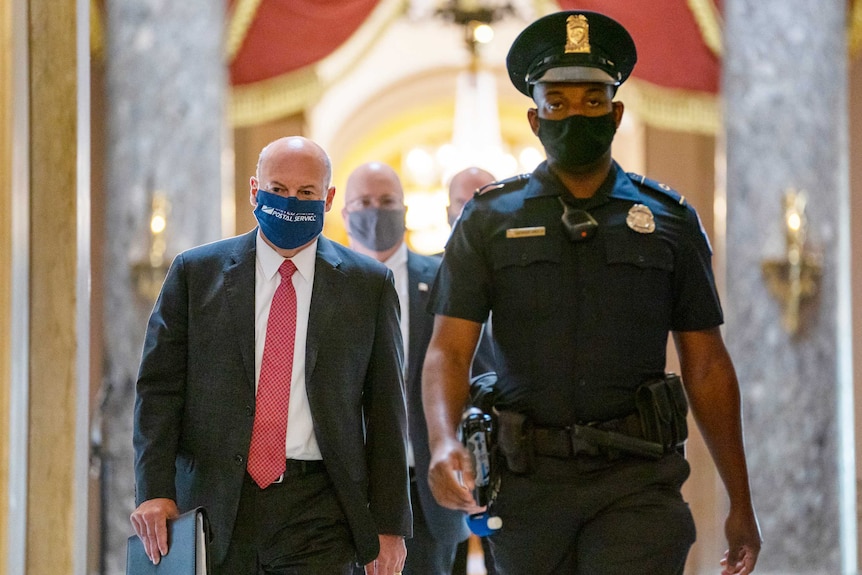 Louis DeJoy walks with a security guard wearing a mask