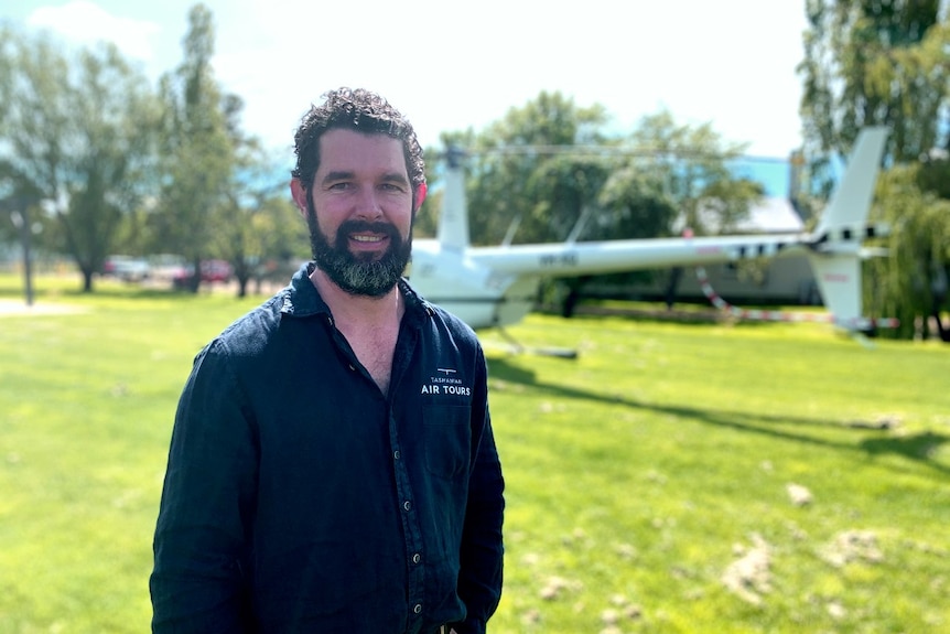 A man stands in front of a helicopter