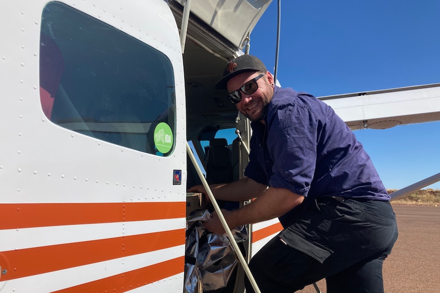 A man stands next to a small plane getting something out