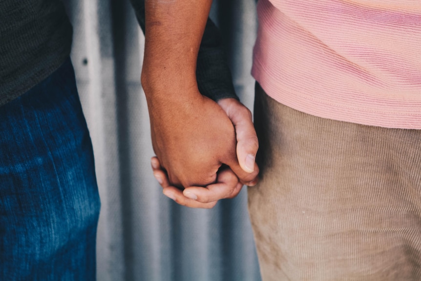 Close up of two men holding hands.