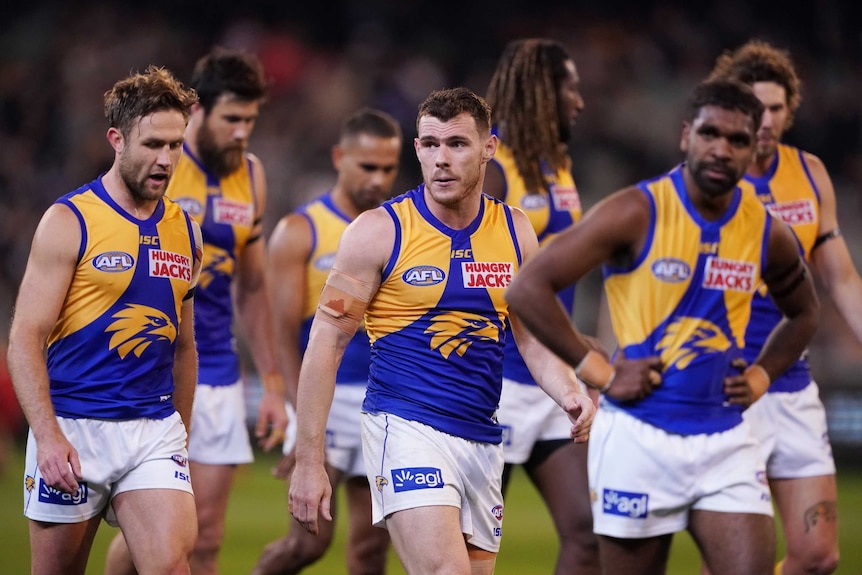A group of West Coast Eagles players look dejected as they walk off the field.