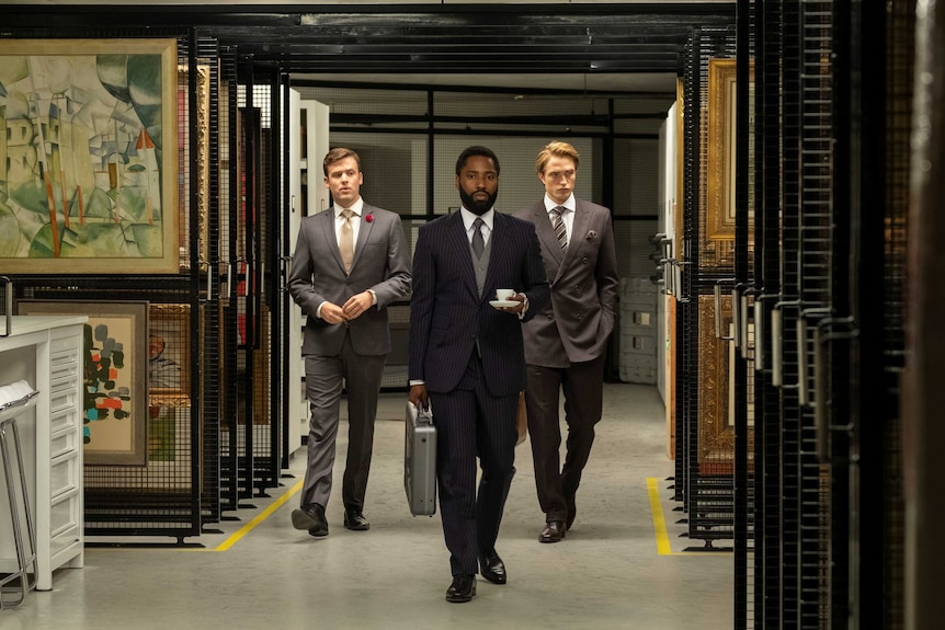 Jack Cutmore, John David Washington and Robert Pattinson walk through a gallery in the film Tenet