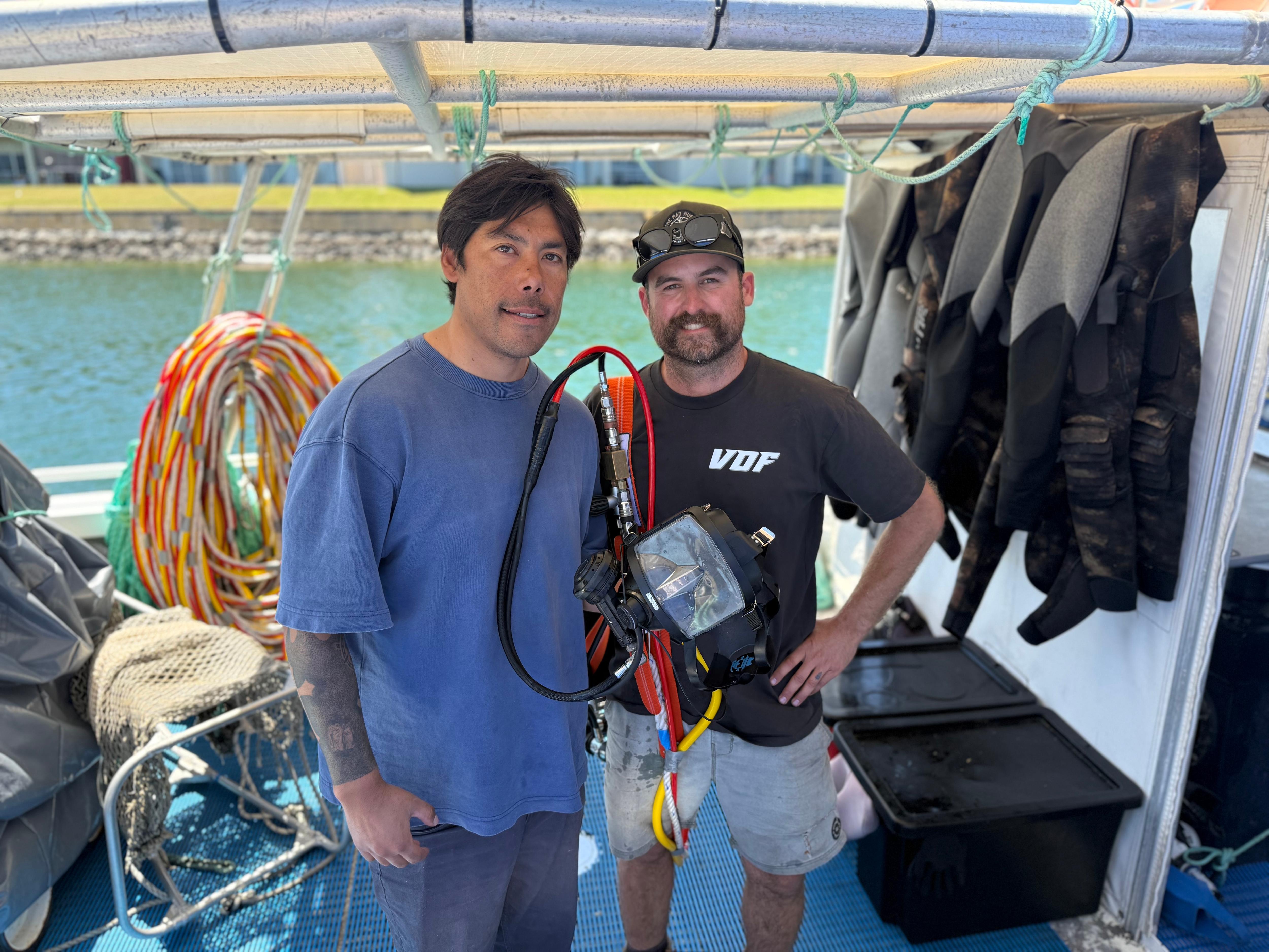 Two dark-haired men, one with a handlebar moustache, standing on a fishing boat.
