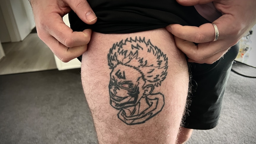 a man shows off a line tattoo of an anime character on his leg