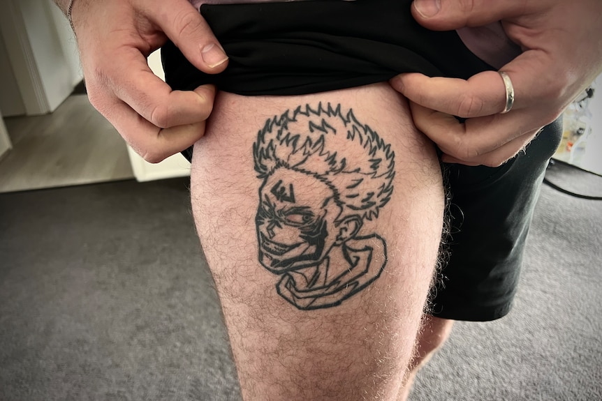 a man shows off a line tattoo of an anime character on his leg