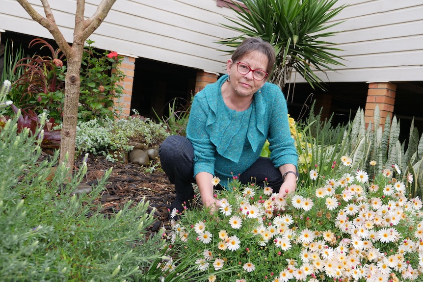 An older woman crouches down next to flowers in a garden.