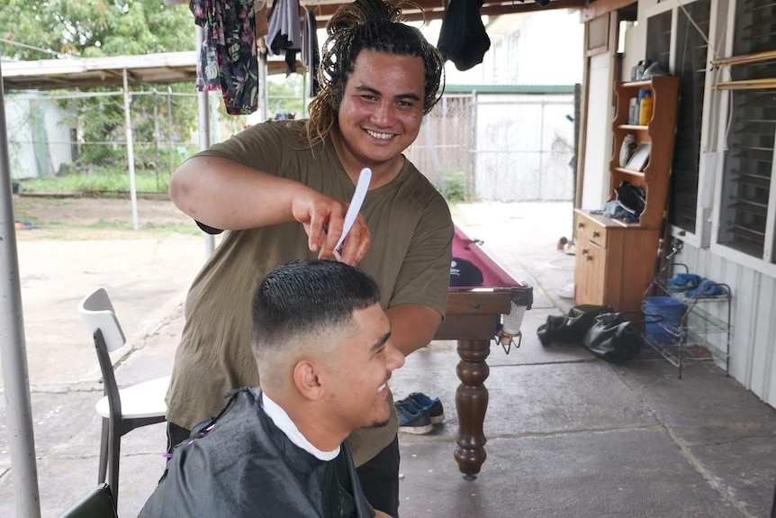 A man with a weave holds a cut-throat razor as he cuts a teenager's hair