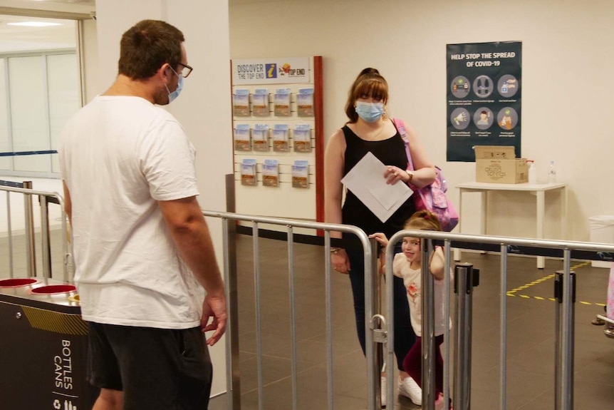 A man is separated by a barrier from his wife and daughter at an airport.