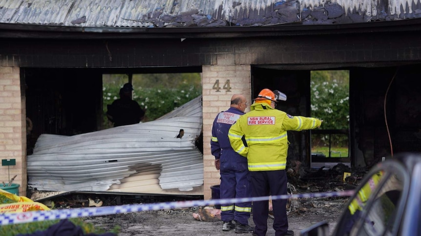 Emergency personnel stand in the burnt-out shell of a house.