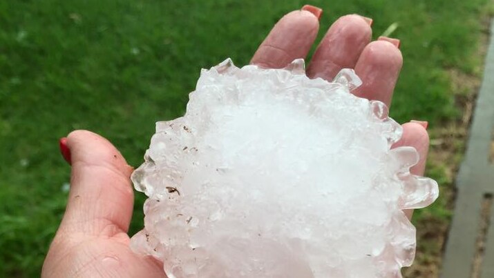 A woman's hand holds a huge jagged piece of hail.
