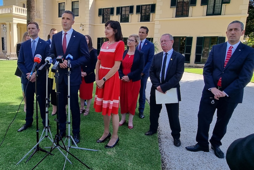 A group of people wearing suits and dresses on a lawn in front of an old house