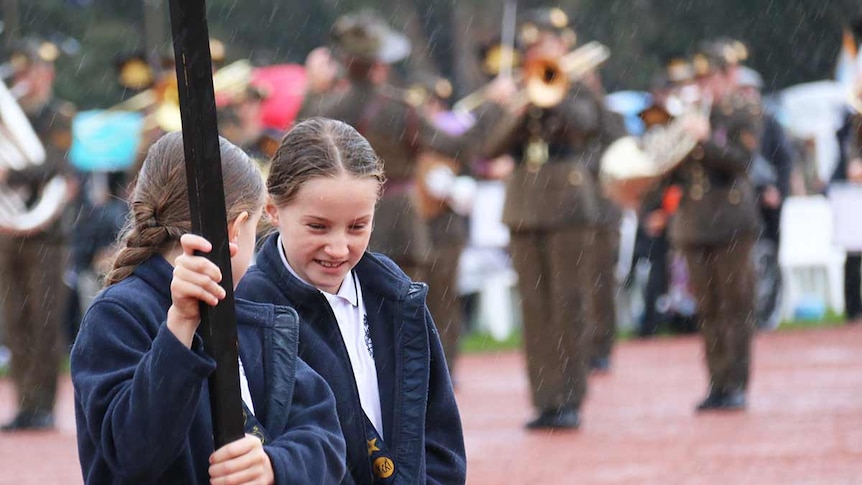 Two girls holding a sign march in the Anzac parade in Canberra in the rain.