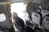 A panel is missing from the side of an aircraft between two rows of passenger seats.