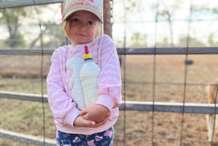 Jodie Muntelwit's small daughter holding a large bottle of animal milk, fence and animal yard in the background