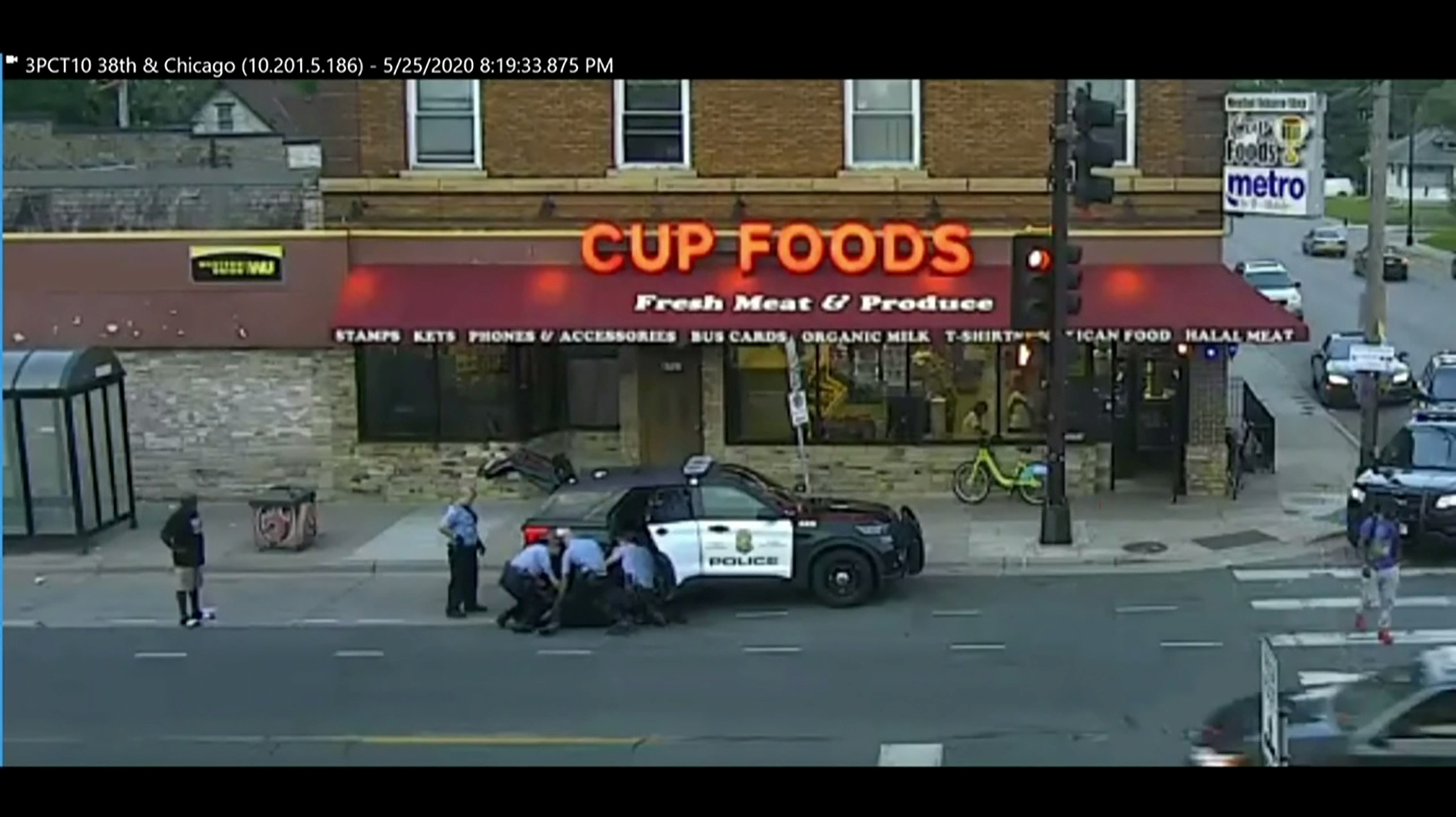 Three police officers pin down George Floyd next to a police car.