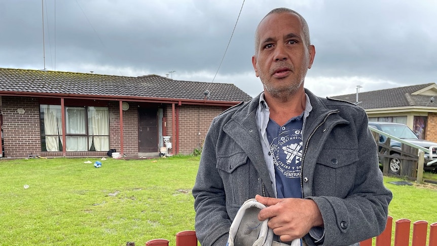 A man stands next to a fence with his joggers in his hand.