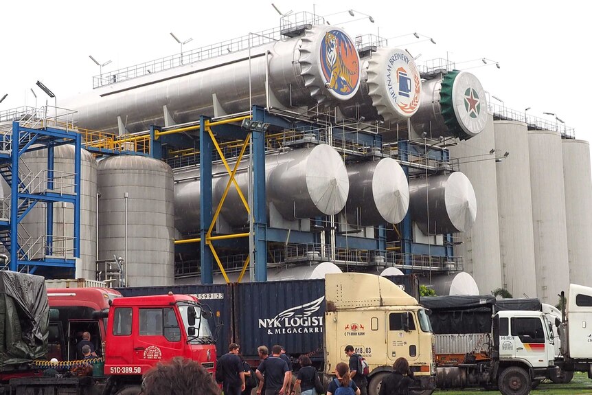 A Heineken beer facility in Vietnam with large vats in the background and trucks in the foreground.