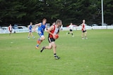 Football players run across an oval. The middle player is holding the ball.