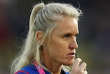 A Western Bulldogs AFLW coach stares to her left as she holds her glasses.