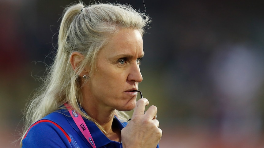 A Western Bulldogs AFLW coach stares to her left as she holds her glasses.